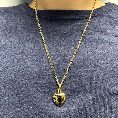 Gold heart cremation necklace for ashes worn on a gray shirt
